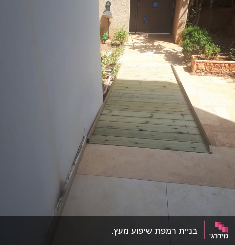 שביל עץ בגינה ליד קיר לבן